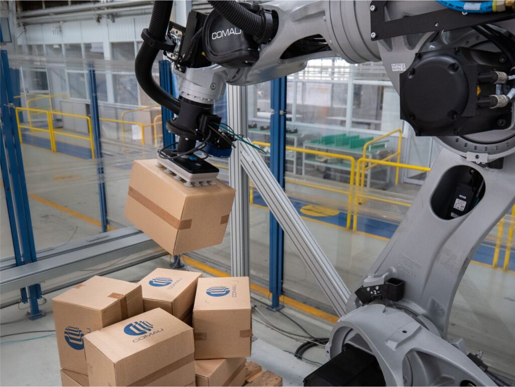 grey Comau robot with gripper handing boxes
